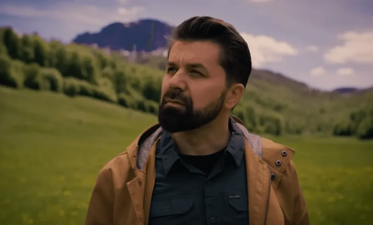 Muškarac sa bradom gleda u daljinu u zelenoj dolini.