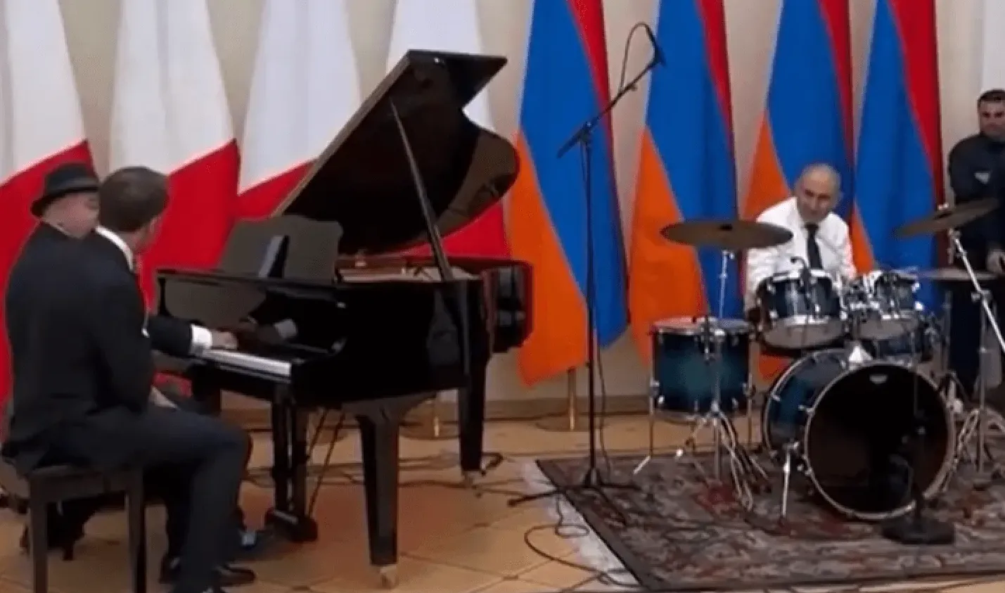 Dvojica muškaraca sviraju klavir i bubnjeve, iza njih se nalaze zastave Italije i Armenije.
