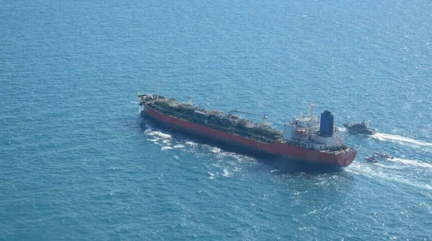 Veliki naftni tanker crvene boje sa bijelom nadgradnjom plovi plavim morem, a uz njega su tri manja broda.