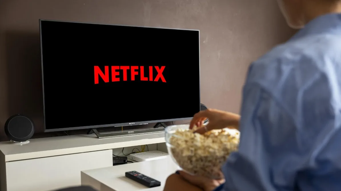 Osoba gleda Netflix na televizoru dok jede kokice iz činije.