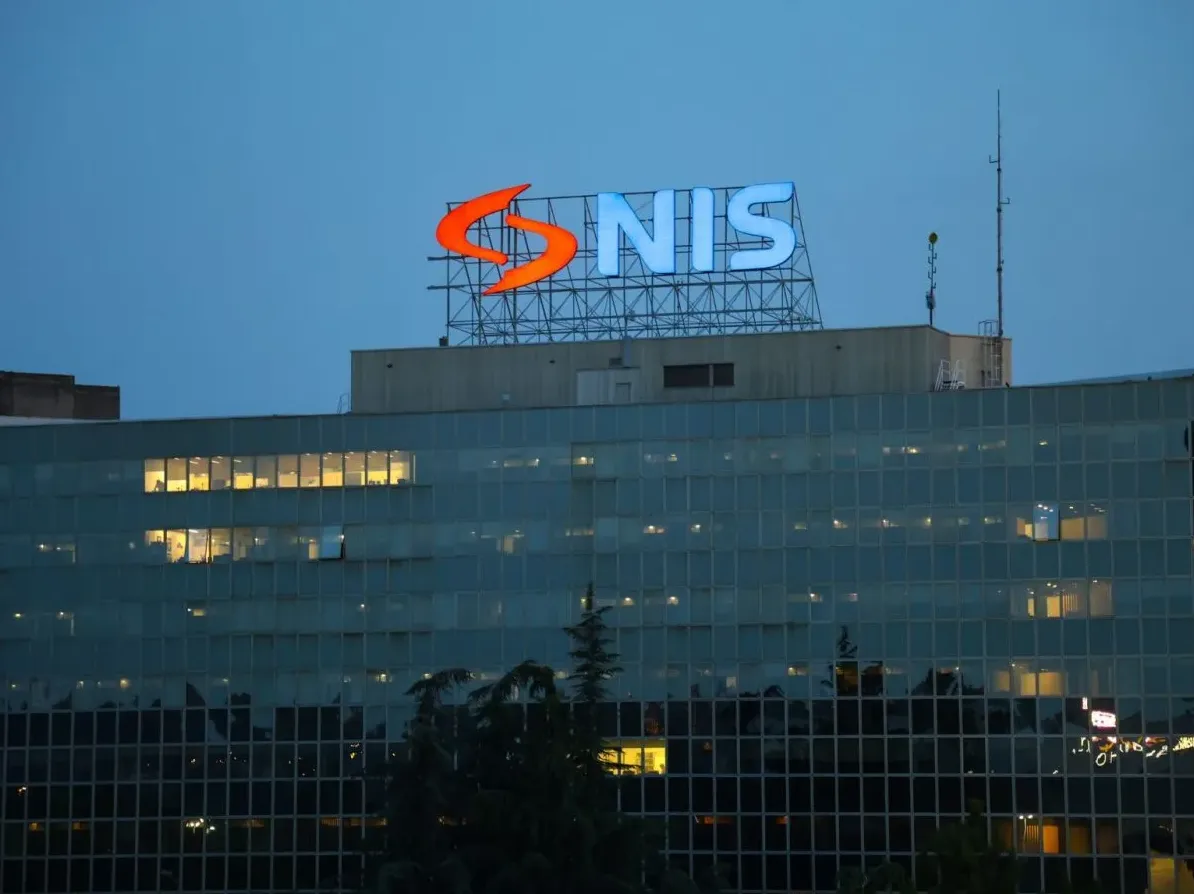 Zgrada sa osvijetljenim prozorima i velikim osvijetljenim logotipom NIS-a na vrhu, u večernjim satima.