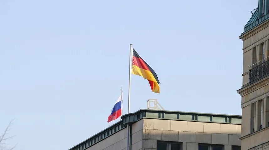 Njemačka i ruska zastava vijore se na vrhu zgrade na plavom nebu.