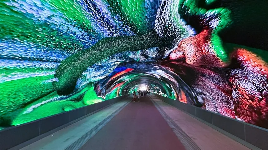 Osvijetljeni tunel sa šarenim, teksturiranim uzorcima koji se protežu duž zidova i svoda, stvarajući iluziju dubine i pokreta.