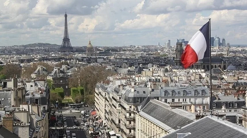 Panoramski pogled na Pariz sa Ajfelovom kulom u daljini i istaknutom francuskom zastavom u prvom planu.