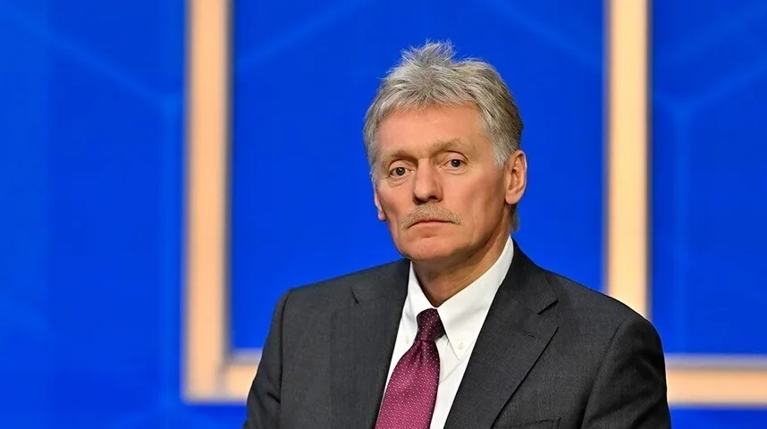 Dmitrij Peskov u tamnom odijelu, bijeloj košulji i sa bordo kravatom sa tačkastim uzorkom, gleda prema kameri.