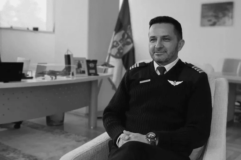 Pilot u uniformi sjedi u stolici u uredu, ispred njega je zastava.