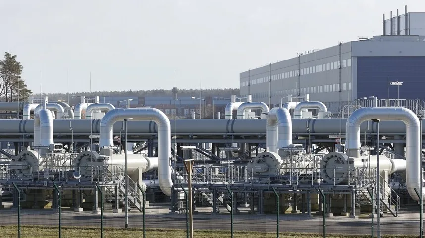 Kompresorska stanica plinovoda sa složenim sistemom metalnih cijevi, ventila i opreme, sa industrijskom zgradom u pozadini.
