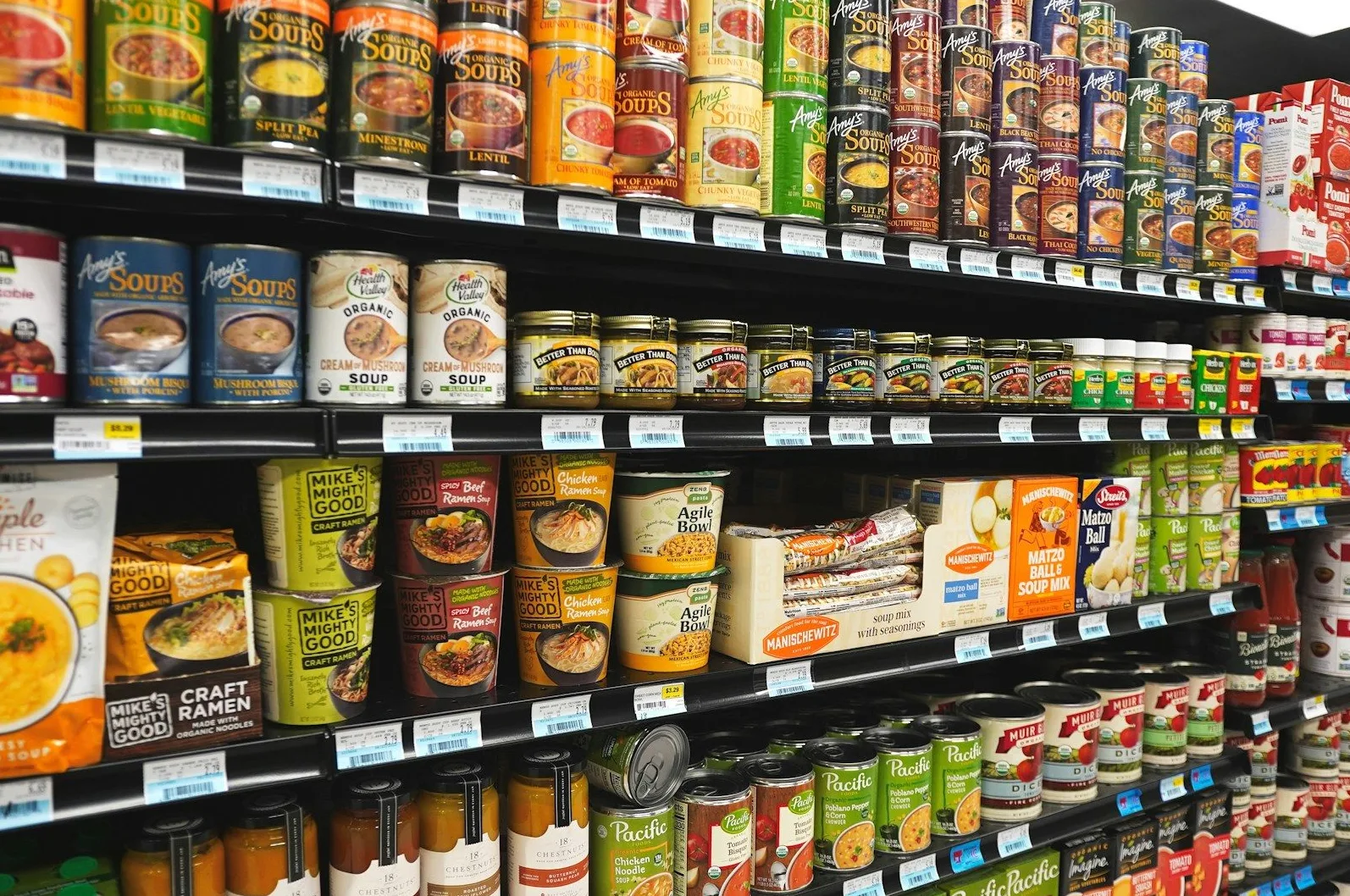 Fotografija prikazuje mnoštvo konzervi i pakovanja supa i drugih prehrambenih proizvoda izloženih na policama supermarketa.