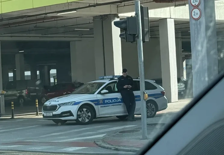 Policajac naslonjen na službeno vozilo policije u podzemnoj garaži.