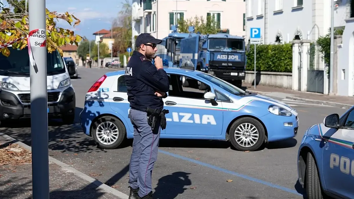 Policajac u uniformi stoji pored plavog službenog automobila marke Fiat sa natpisom "POLIZIA" na boku.