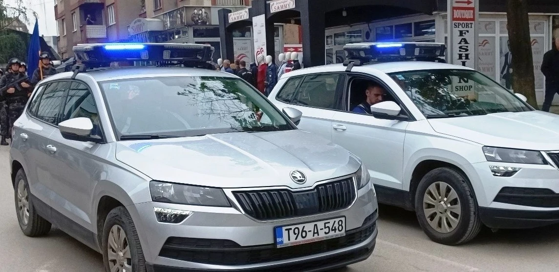 Dva policijska automobila marke Škoda sa uključenim rotacionim svjetlima na ulici ispred prodavnica.