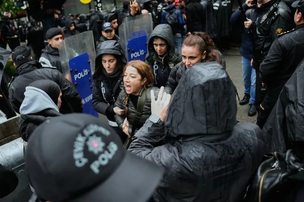 Žena viče tokom policijske intervencije na protestu, dok je policajci drže
