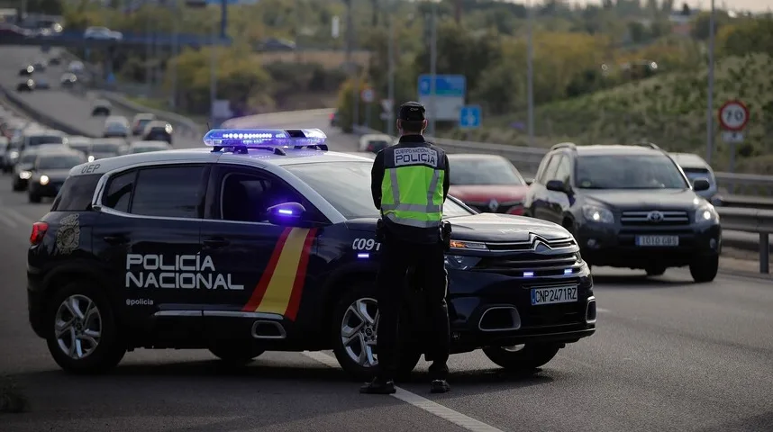 Policijski službenik Nacionalne policije u reflektujućem prsluku stoji pored policijskog automobila sa uključenim plavim svjetlima na kontrolnoj tački na autoputu.