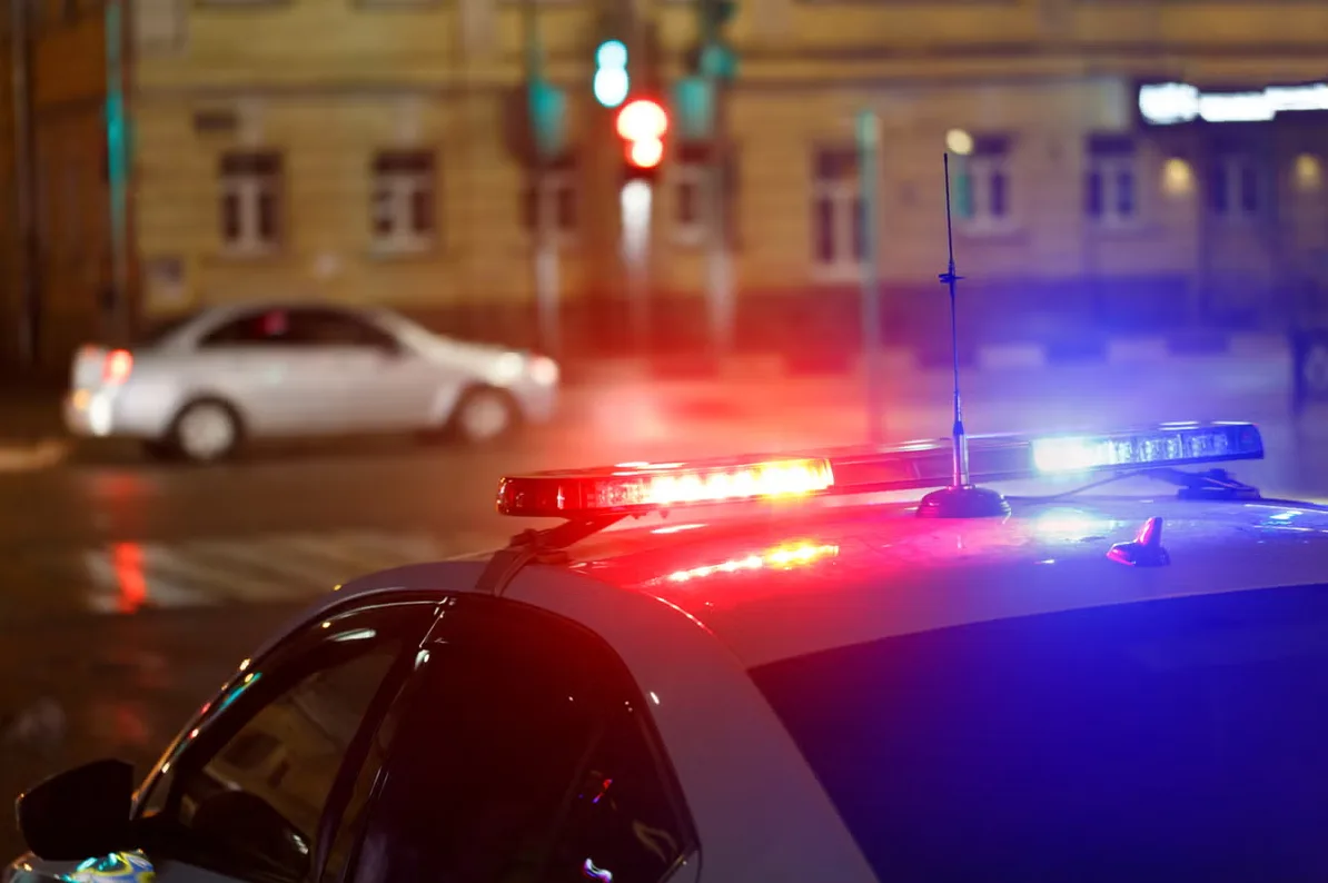 Policijsko vozilo s upaljenom crvenom i plavom rotacijom na krovu, u noćnom okruženju grada.
