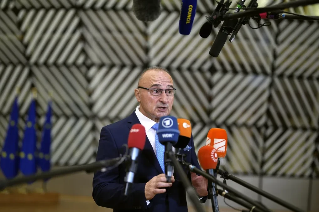 Političar u tamnom odijelu i plavoj kravati govori pred mnoštvom mikrofona sa logotipima raznih medija, uključujući ORF, WDR i France Info, u prostoriji sa zastavama Evropske unije i grafičkim uzorkom na zidu.