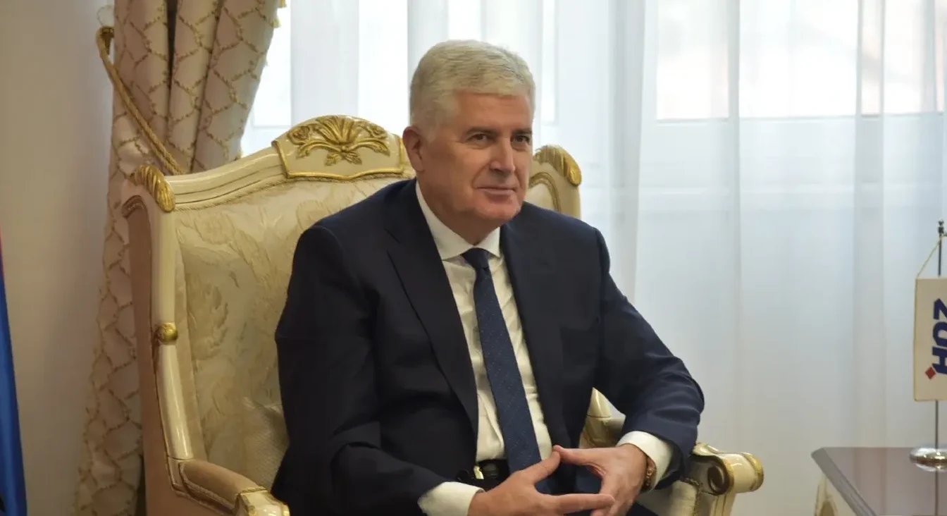 Dragan Čović u tamnom odijelu i plavoj kravati sjedi na raskošnoj fotelji pored zastavice sa logom HDZ-a.