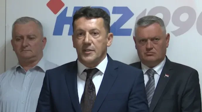 Troje muškaraca u odijelima ispred logotipa HDZ-a.