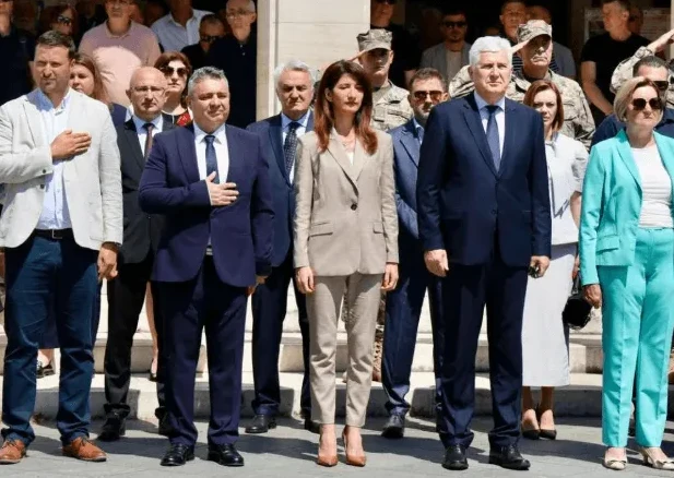 Grupa političara i zvaničnika stoji u formaciji napolju, sa rukama na grudima u znaku poštovanja.