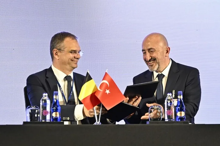 Dva muškarca potpisuju dokument, sa zastavama Belgije i Turske pored njih.
