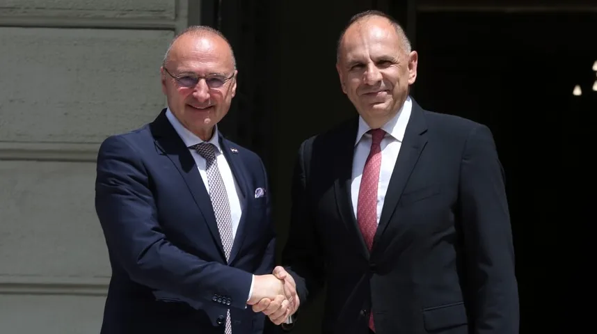 Dva muškarca u odijelima rukuju se ispred zgrade.