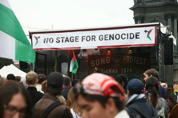 Skupina ljudi na protestu ispred bine sa transparentom "NO STAGE FOR GENOCIDE"