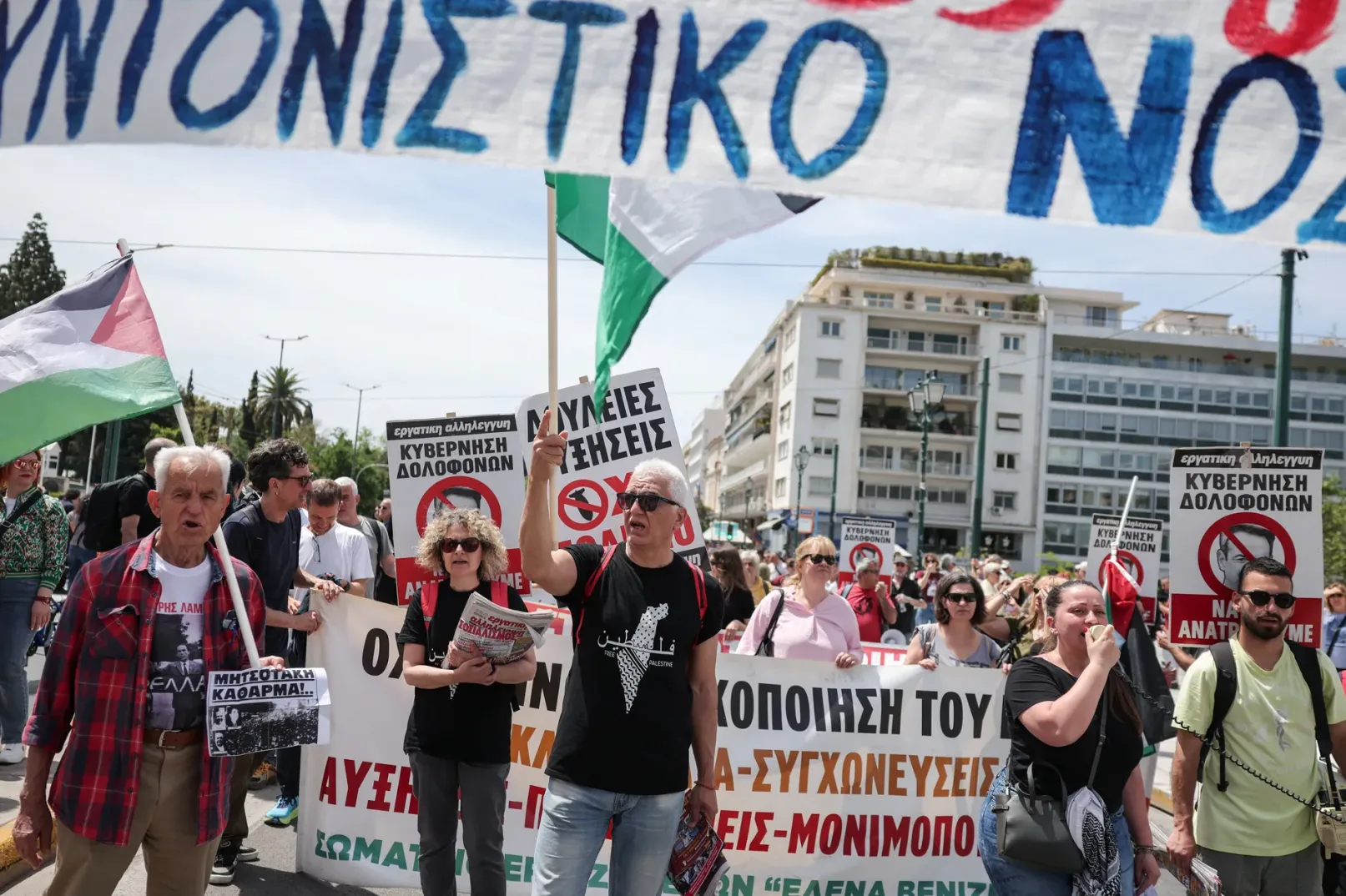 Grupa ljudi na protestu drži palestinsku zastavu i transparente na grčkom jeziku.
