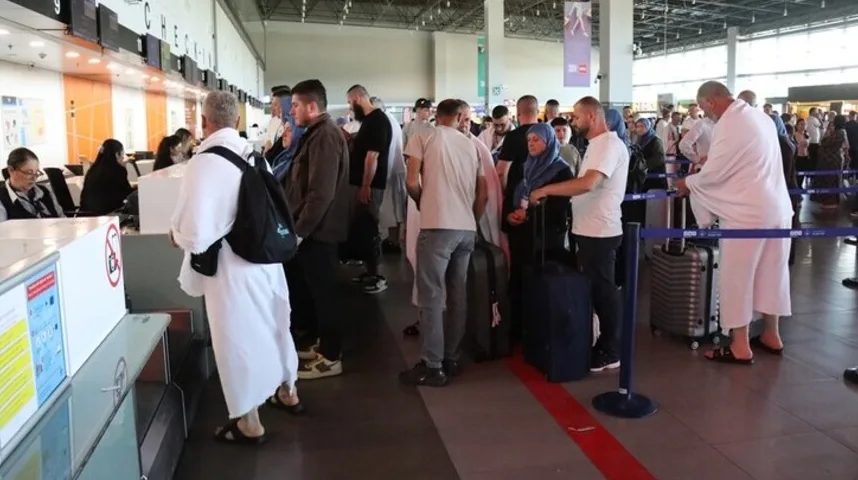 Putnici u bijelim ihranima čekaju u redu na aerodromskom šalteru za prijavu, noseći prtljag i torbe.