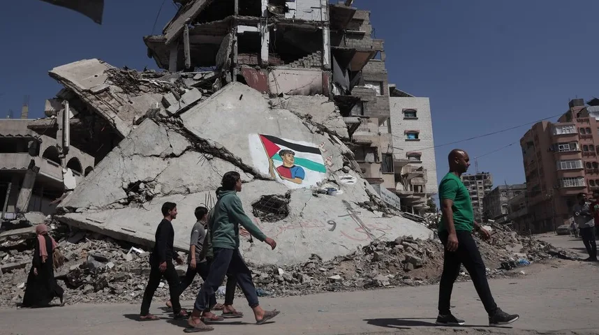 Ljudska grupa prolazi pored razorene zgrade sa palestinskom zastavom i portretom dječaka naslikanim na zidu.
