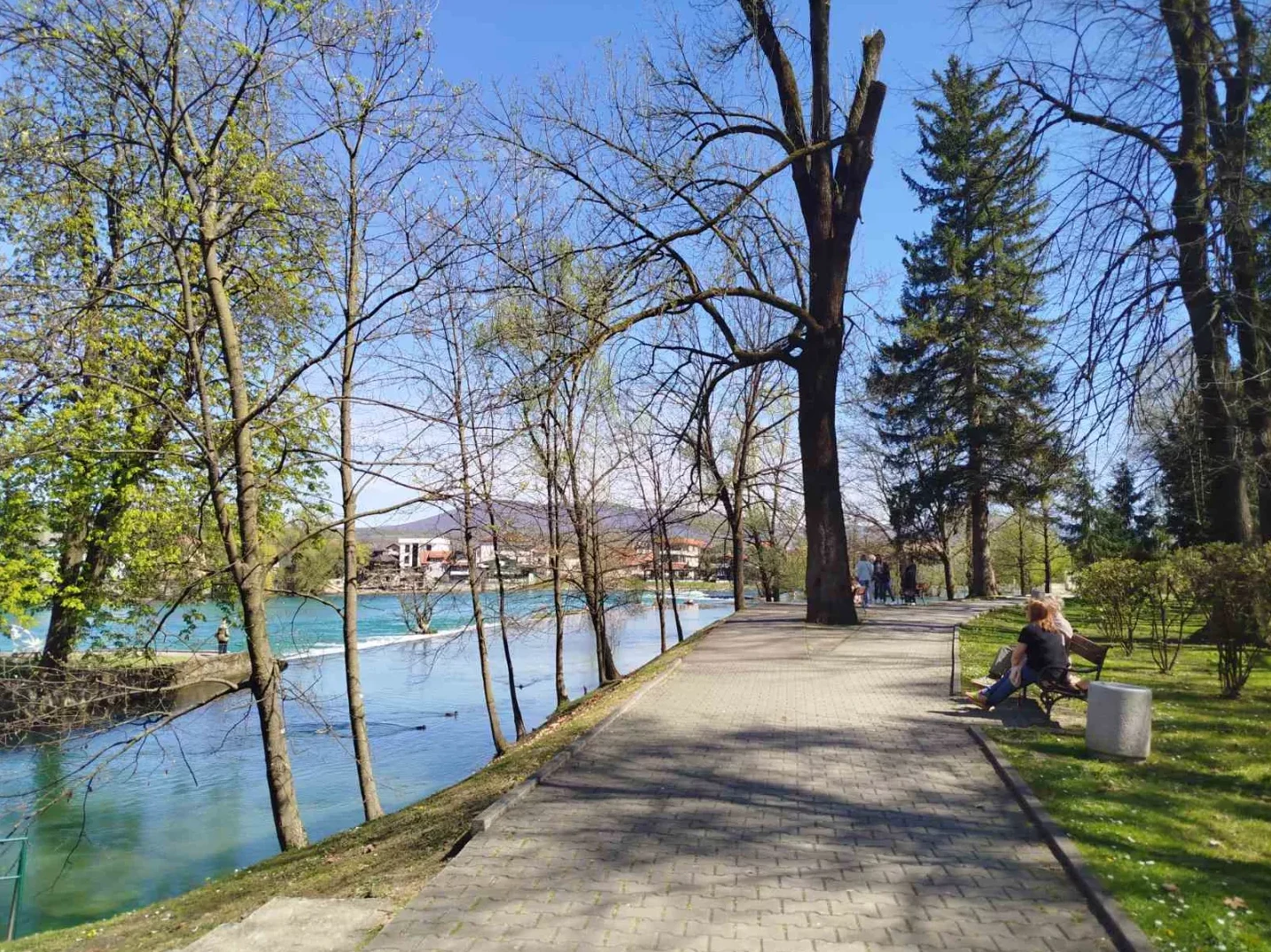 Šetalište pored rijeke s drvećem i ljudima na klupi