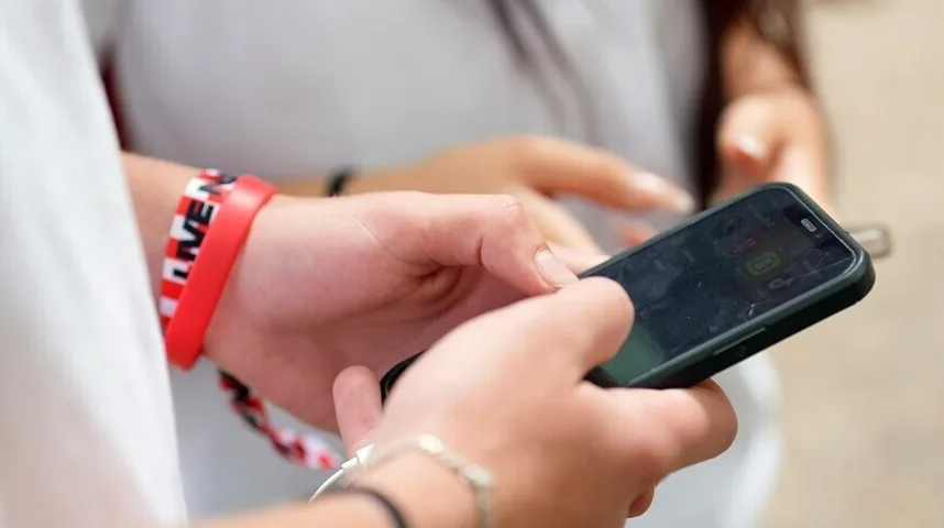 Mlada osoba drži pametni telefon i koristi ga prstima, na ruci nosi crvenu narukvicu s bijelim i crnim uzorkom i nekoliko drugih narukvica.