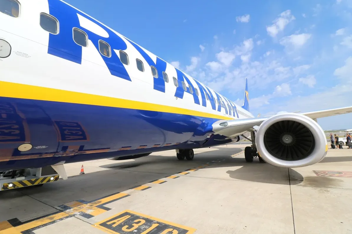 Detaljan pogled na trup Ryanairovog aviona s plavom i žutom trakom, kao i na njegov moćni mlazni motor na aerodromskom terminalu.