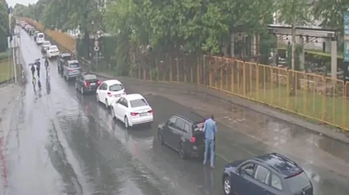 Saobraćajna gužva u deset kolona tokom kišnog dana, gdje osoba pretovara stvari iz prtljažnika automobila.