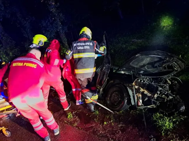Saobraćajna nesreća noću, vatrogasci i hitna pomoć intervenišu pored teže oštećenog automobila.