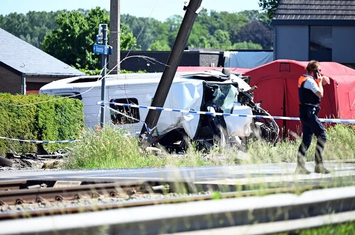 Teško oštećeno vozilo nakon saobraćajne nesreće u blizini željezničke pruge, sa crvenim šatorima i policijskim službenikom na licu mjesta.