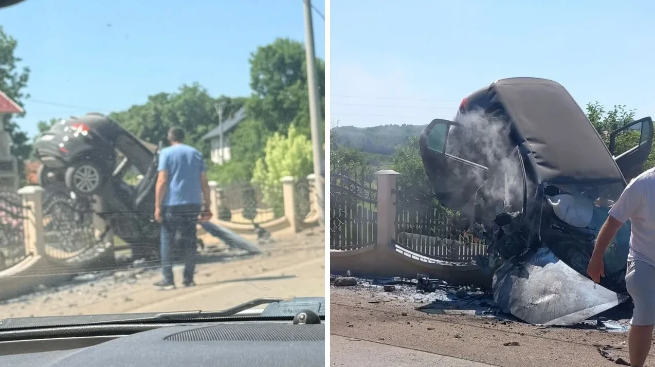 Automobil prevrnut na ogradu nakon saobraćajne nesreće, sa vidljivim dimom i oštećenjima.