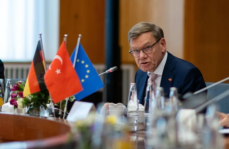 Političar sa naočarima govori za stolom ispred zastava Njemačke, Turske i Evropske unije.