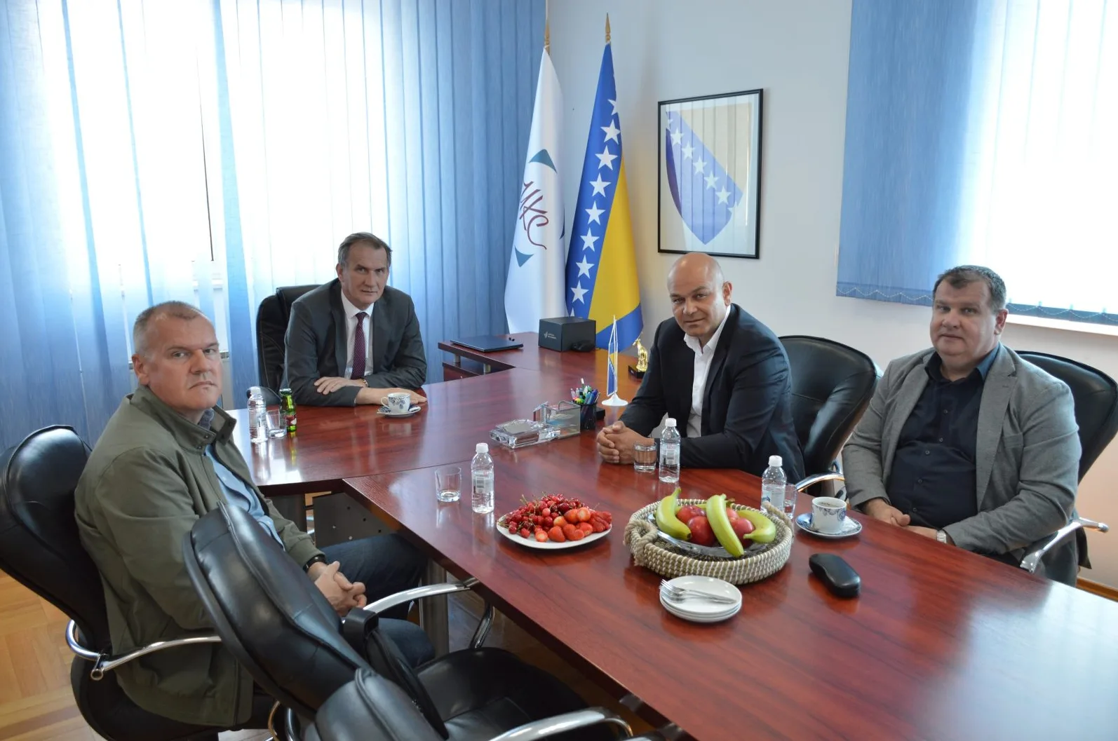 Četiri muškarca sjede za drvenim stolom u kancelariji sa zastavama Bosne i Hercegovine.
