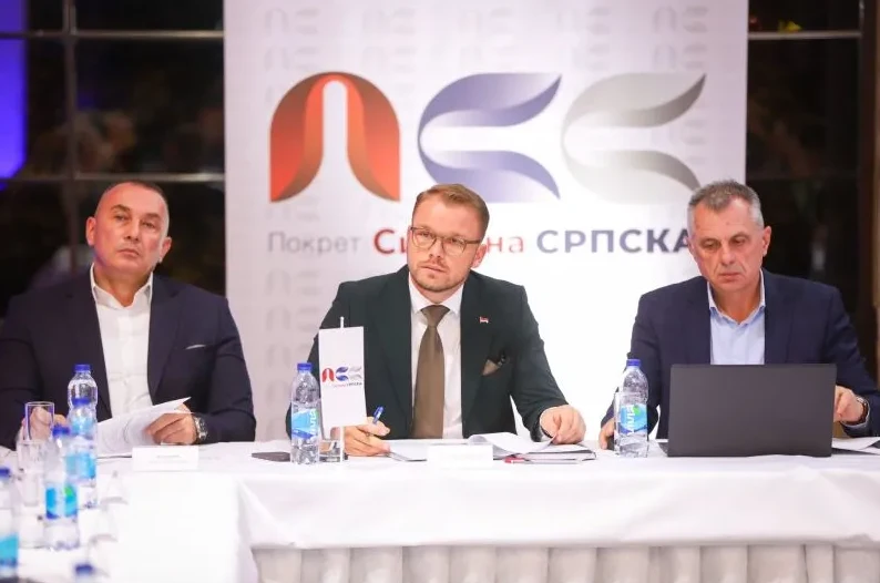 Tri muškarca sjede za stolom ispred natpisa "Pokret Snaga Srpske".