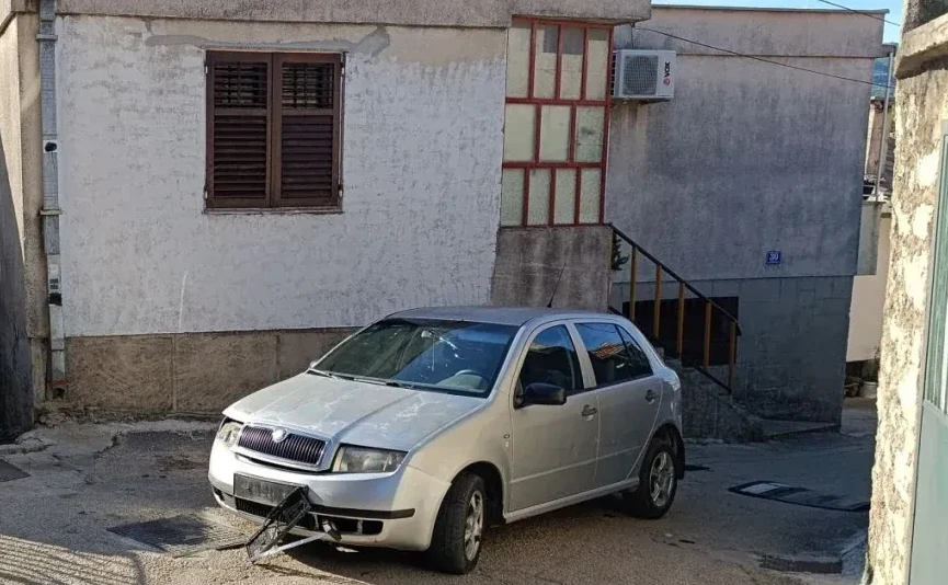 Srebrna Škoda Fabia sa oštećenim prednjim branikom parkirana ispred zgrade