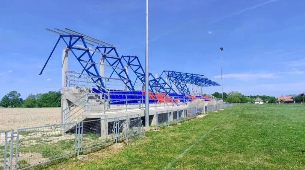 Tribine sportskog stadiona sa plavim i crvenim sjedalicama pod plavim nebom.