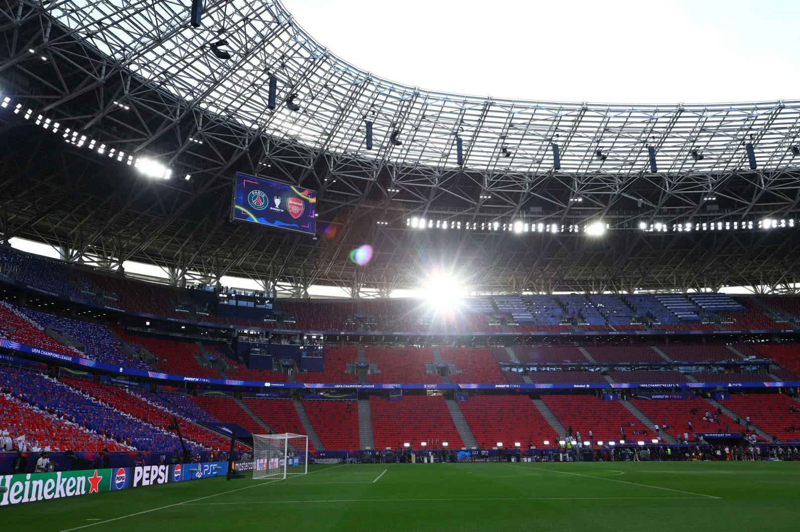 Tribine stadiona ispunjene navijačima u crvenim i plavim bojama, sa velikim ekranom iznad terena.