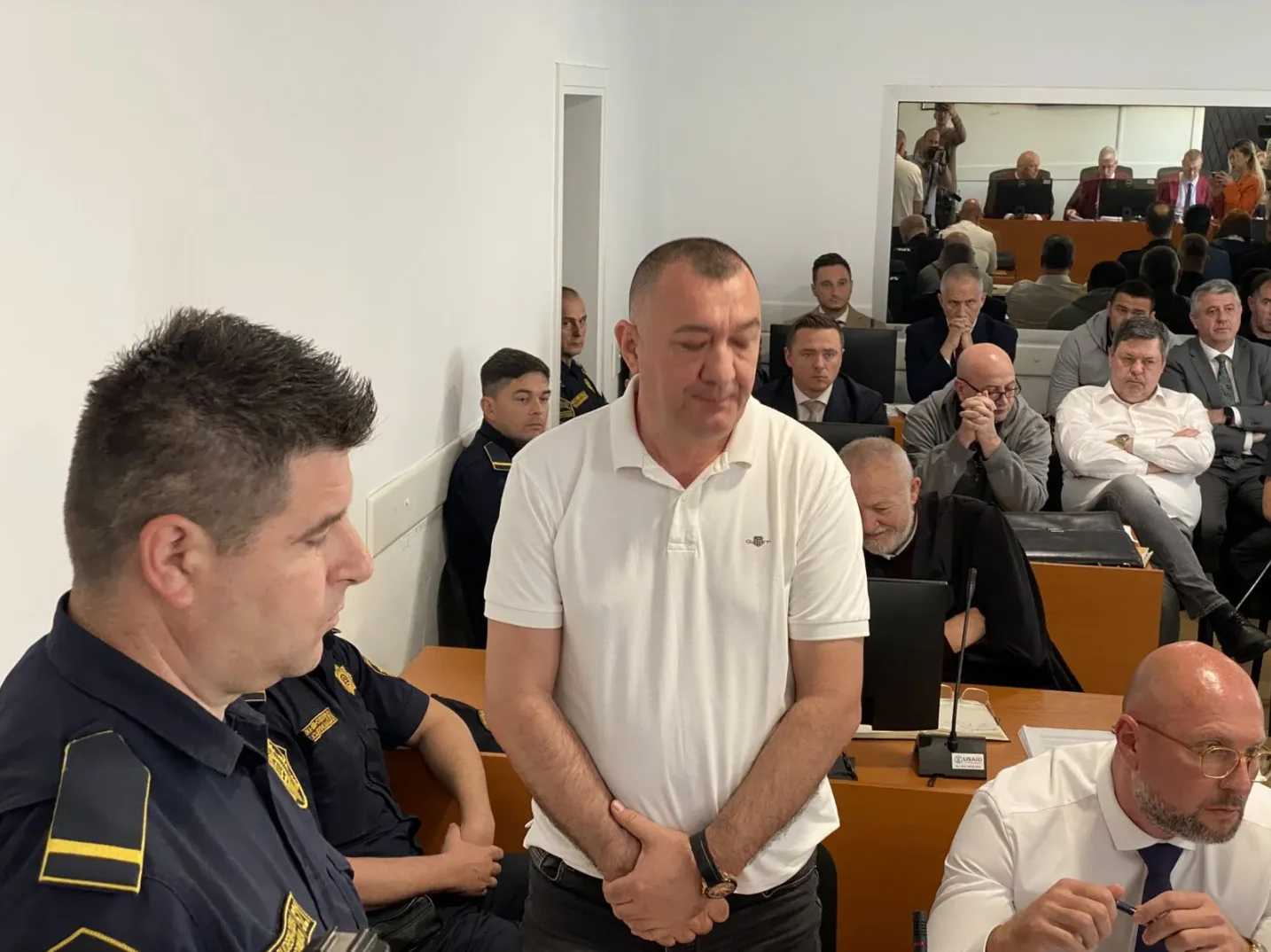 Optuženi stoje pred sudijama dok policajci stoje u pozadini.
