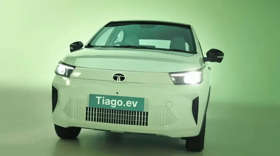 Prednji dio bijelog električnog automobila Tata Tiago.ev sa uključenim farovima.