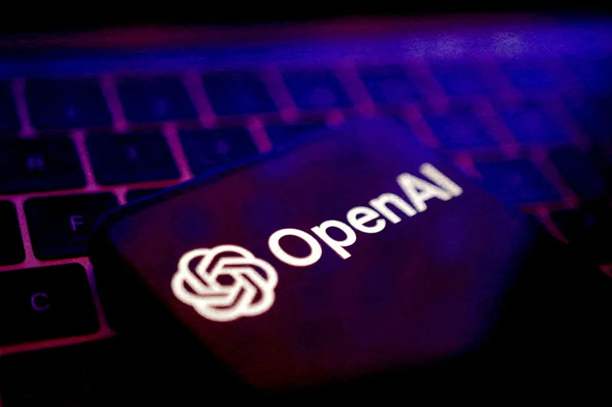 Telefon sa osvijetljenim logom "OpenAI" na ekranu, položen preko tamne tastature sa ljubičastim pozadinskim osvjetljenjem.