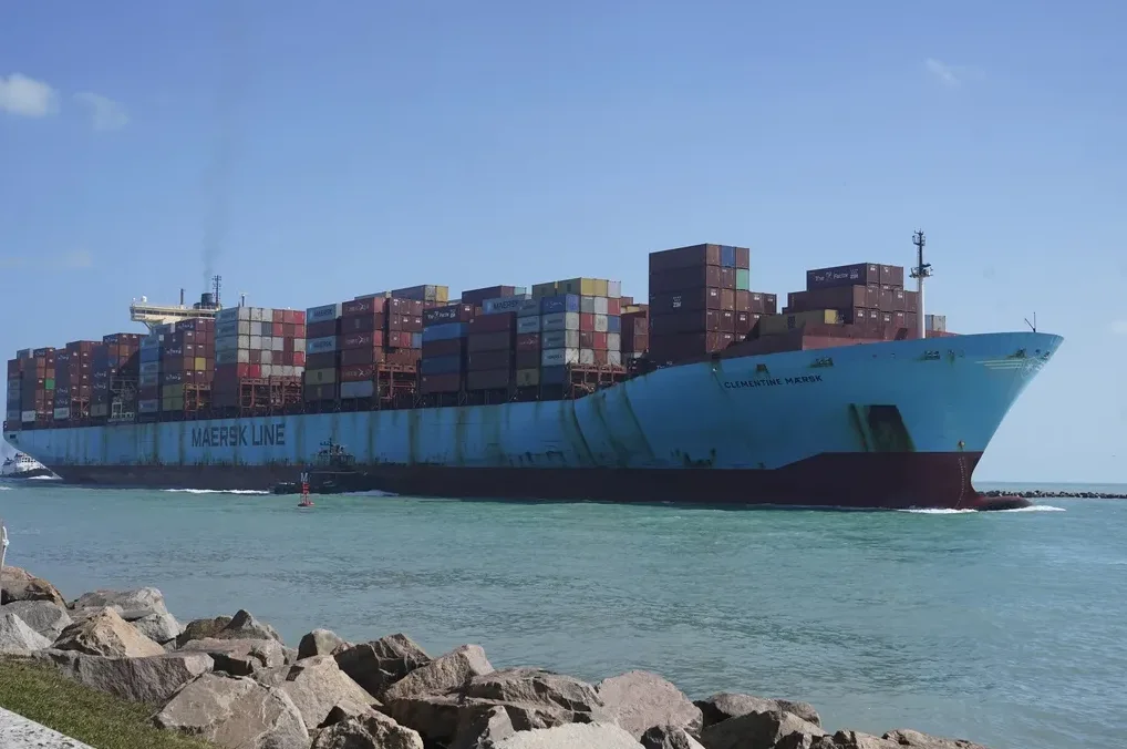 Ogroman teretni brod 'Clementine Maersk' sa mnoštvom kontejnera na palubi plovi plavim morem pod vedrim nebom.