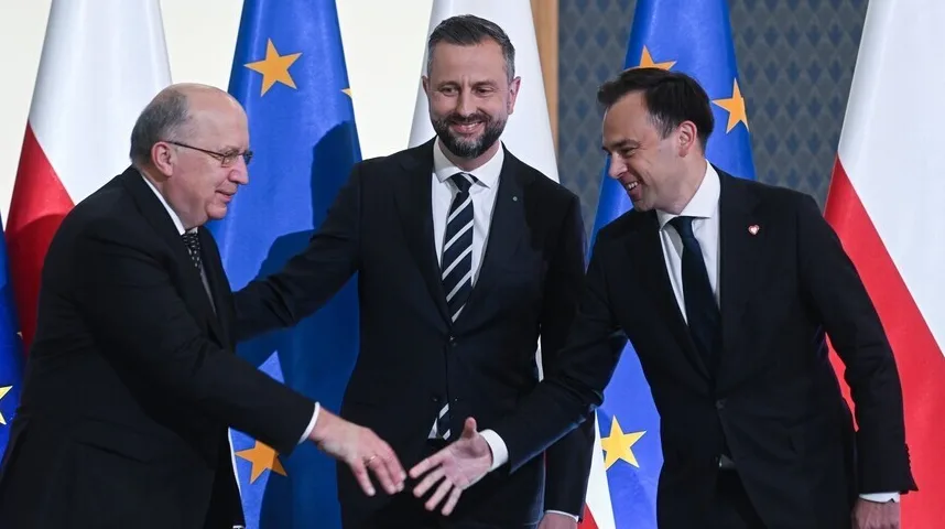 Tri muškarca u odijelima rukuju se ispred zastava Evropske unije i Poljske.