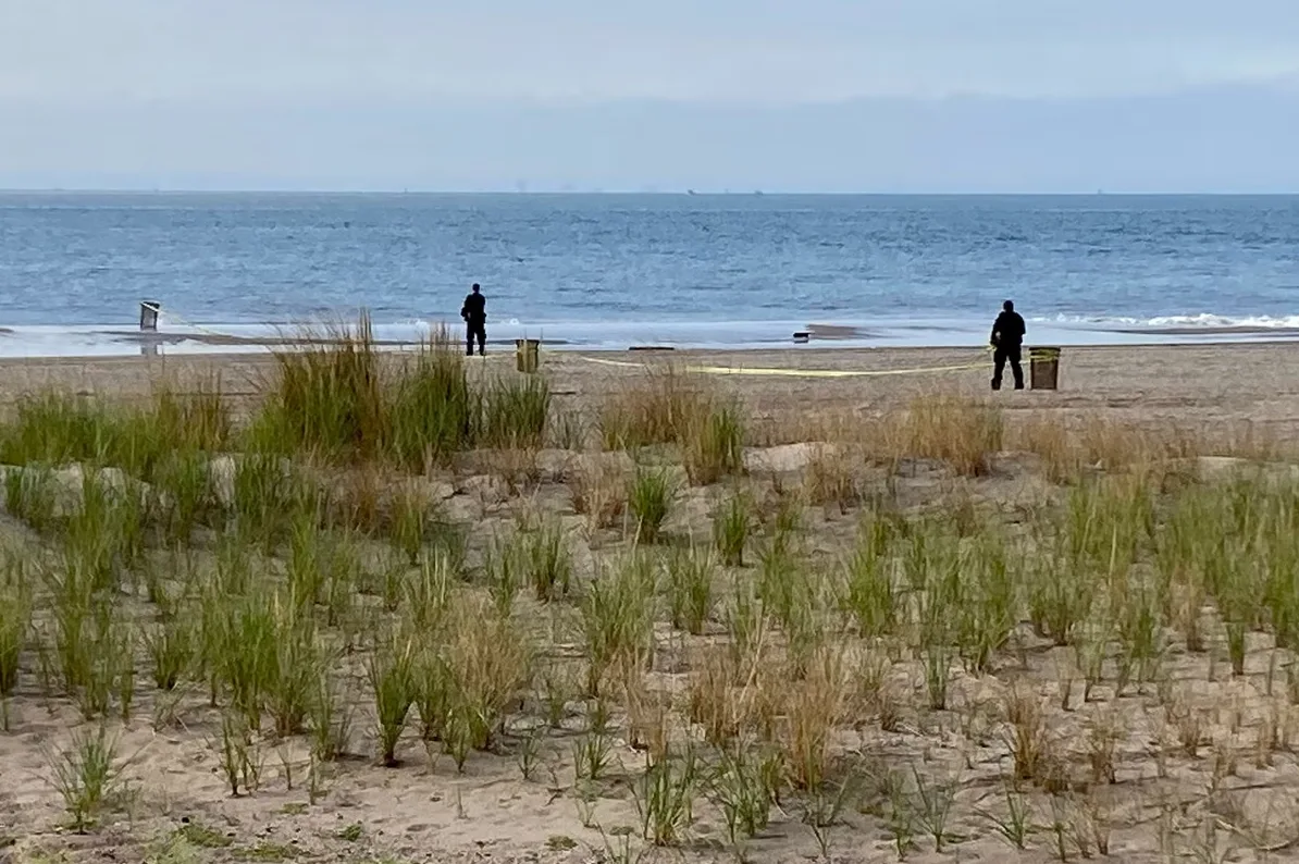 Dva muškarca stoje na plaži, jedan od njih blizu kante za smeće i obavijesne trake.