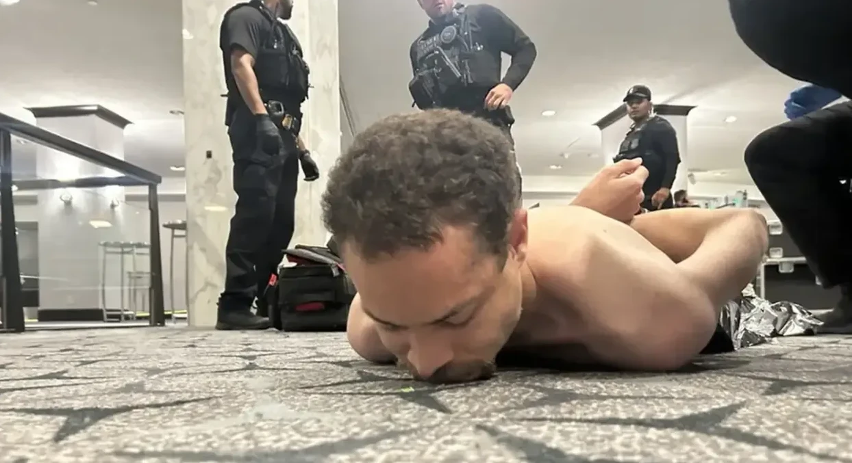Uhapšeni muškarac leži na podu okružen policajcima.