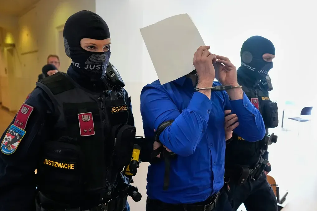 Pripadnici pravosudne policije sprovode optuženika sa lisicama na rukama i papirićem preko lica.