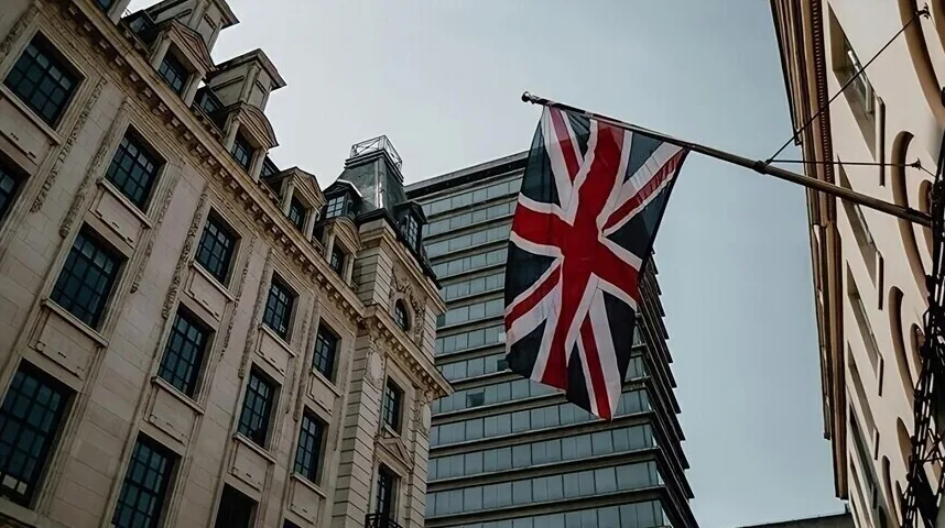 Union Jack zastava Velike Britanije istaknuta na jarbolu između klasične zgrade i moderne zgrade od stakla.